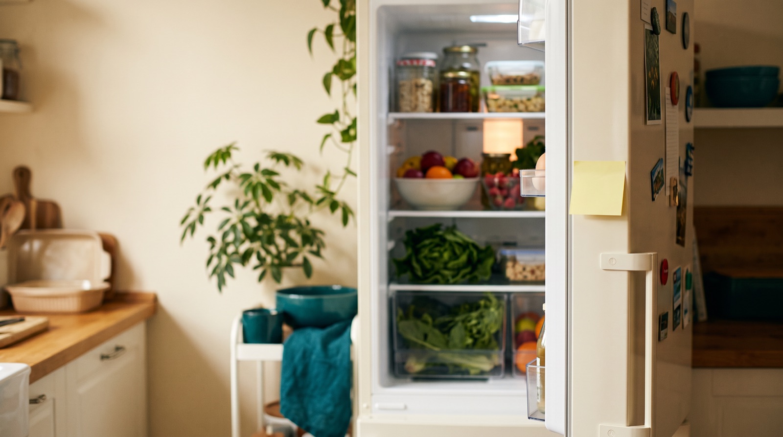 An open refrigerator full of fresh produce with a blank note on the door.