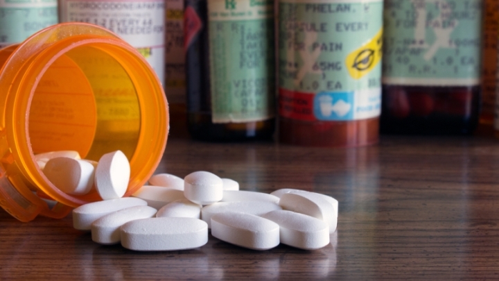 Unidentifiable opioid pills spill out of a prescription bottle.
